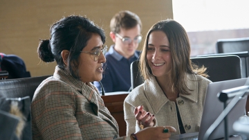 Two students in class speaking with one another