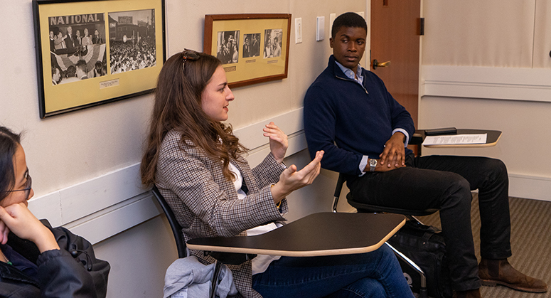 Furman scholar sitting in a classroom speaking, with two other students listening intently