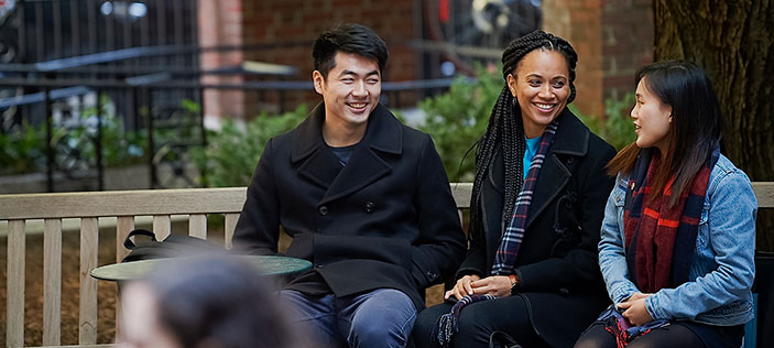 Three students sitting on a bench in courtyard