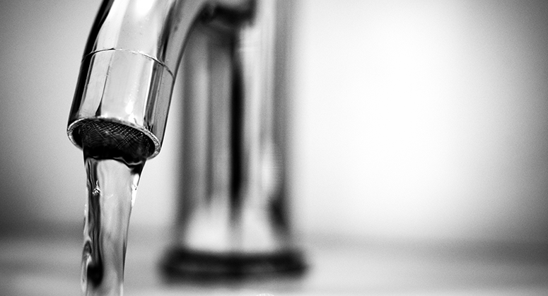A black and white photo of a running faucet.