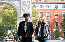 Two women students walking through Washington Square Park in front of arch and row houses