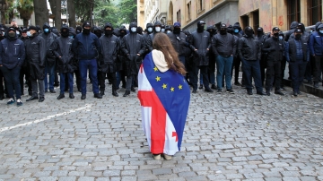A demonstrator with draped Georgian national and EU flags stands in front of police.