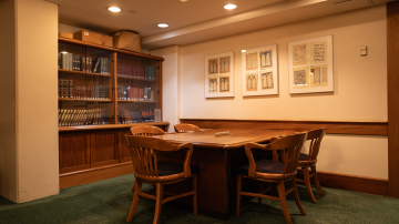 Table surrounded by chairs and with bookshelves and art on the walls