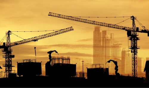 Building construction site with cranes silouhetted at sunset