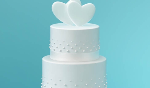 White wedding cake with hearts on top, in front of baby blue background