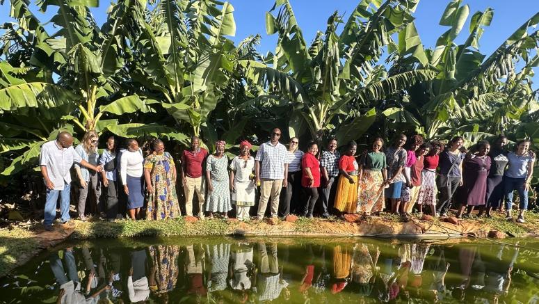 group of people lined up smiling with trees in background and body of water in front