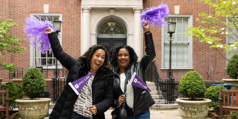 Two alumnae waving purple pom-poms in front of Vanderbilt Hall