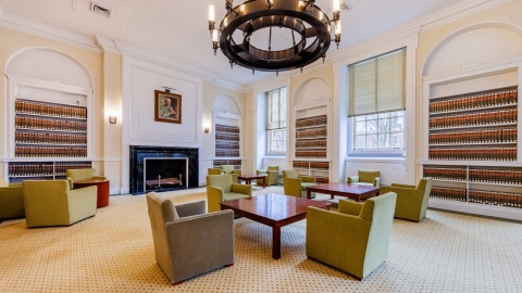 Green chairs around a square table with a chandelier above and a fireplace in the background