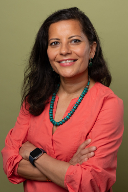 Brown woman with midlength hair wearing a bright shirt and blue necklace