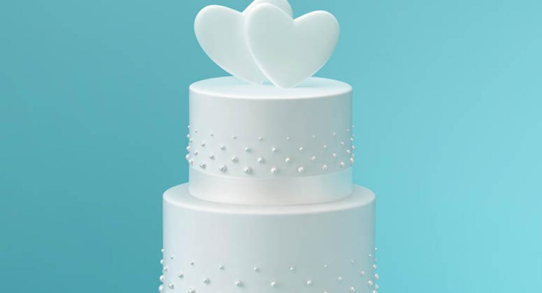 White wedding cake with hearts on top, in front of baby blue background