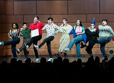 Group of students in a kick line on stage