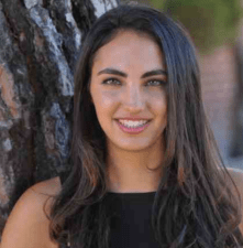 person with long dark hair smiling with a tree in the background