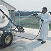 An agricultural worker wearing a white protective suit while spraying chemicals.