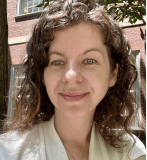 White woman with brown curly hair smiling at camera