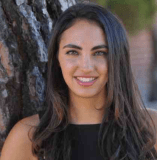 Person with long hair smiling with a tree in the background