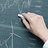 A hand writing on a chalkboard, with illustrations of wind turbines and stock market graphs.