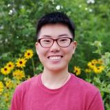 Yimeng in glasses and pink shirt smiling in front of trees and flowers