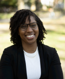 Zakiya wearing glasses and black blazer and white shirt smiling in front of camera