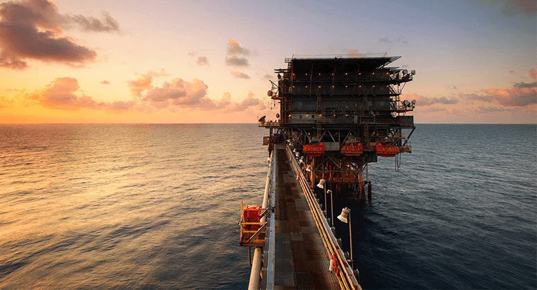 An offshore drilling platform against an orange sunset.