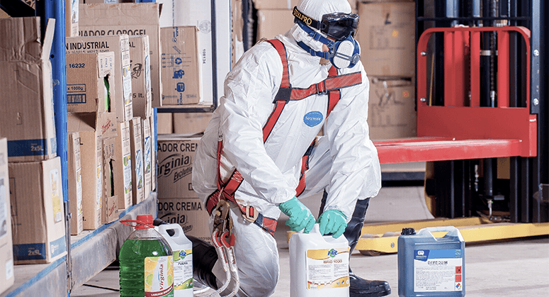 A man wearing protective equipment while handling containers of chemicals.