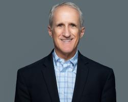 Charles Platt wearing dark nay blazer and blue plaid shirt smiling in front of camera