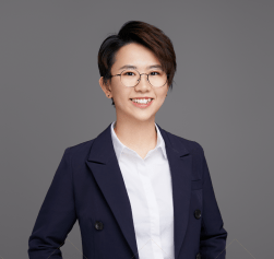 Image of Wenny Shen wearing a navy blazer smiling, standing in front of charcoal grey-colored background